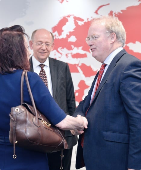 Two men and a woman shaking hands in front of a world map, symbolizing global cooperation and partnership, exemplifying Nedonboard's commitment to international collaboration.